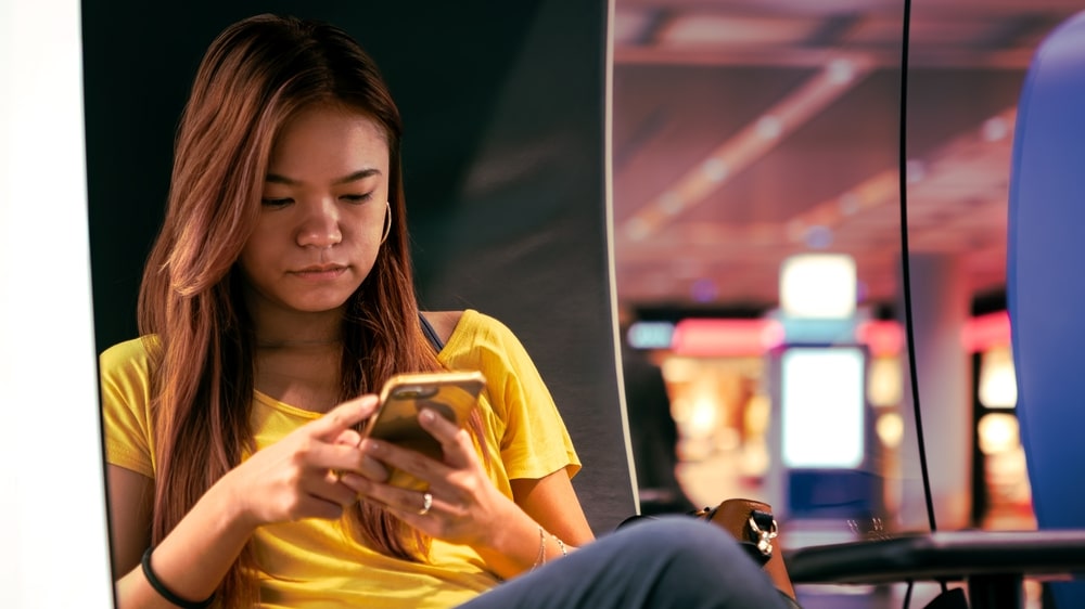 An,Asian,Woman,Traveler,Checks,Her,Phone,While,Seated,In young woman in lounge